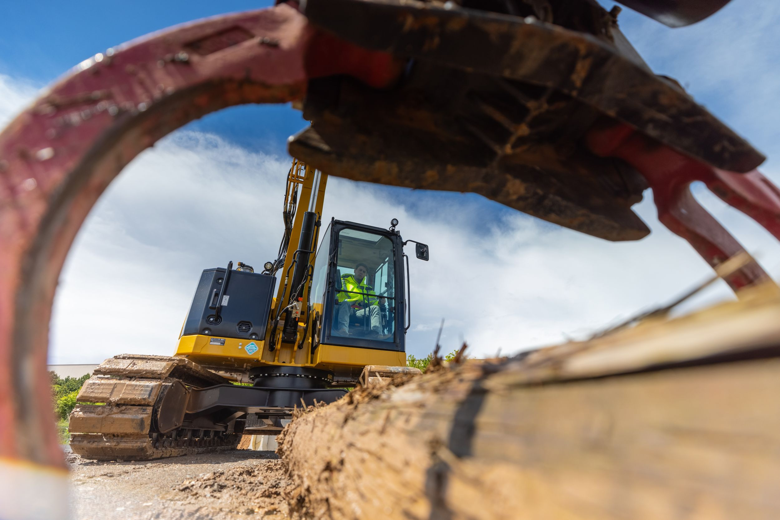 Low angle view of a Cat 308 CR fixed boom mini excavator lifting a log with a grapple at a construction site.