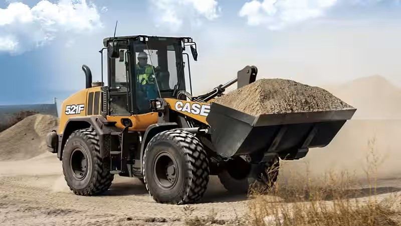 Right side view of a Case 521F Wheel Loader on site hauling material in it's shovel, operator can be seen in the cab.