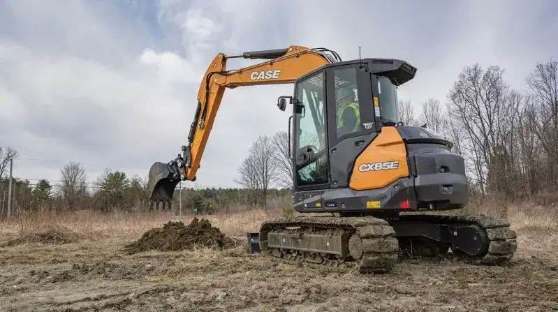 Left side view of a Case CX85E midi size excavator digging in the dirt, the operator can be seen in the cab.