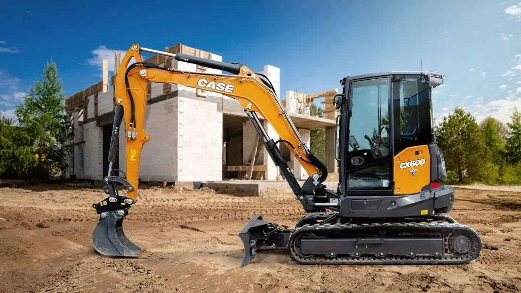 Left side view of a Case CX60D mini size excavator parked on a job site with a partially built white building behind it.