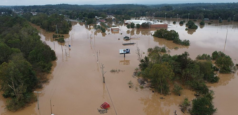 Arial view of a town flooded where buildings, power lines, signs and trees are seen partially submerged in brown water.
