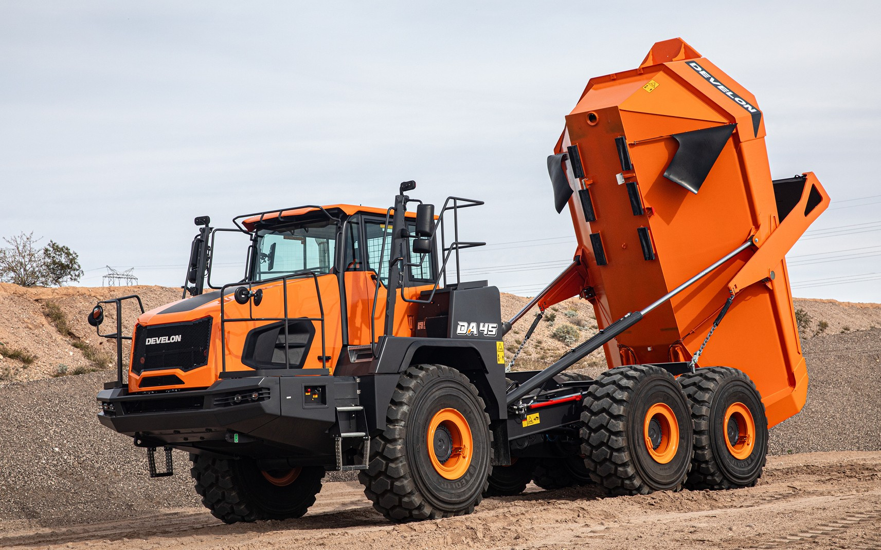 Orange DEVELON DA45-7 articulated dump truck with raised dump body at a job site.