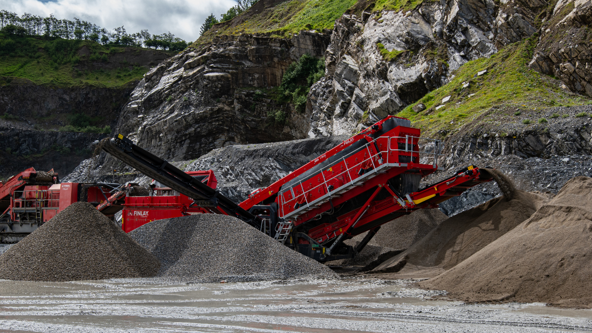 Red Finlay 694 Inclined Screener sorting materials into separate piles near grassy rock hills.