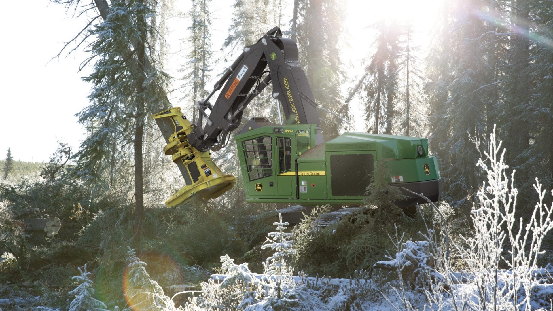 John Deere 953M Buncher cutting down a tree in a forested and snow-covered area.