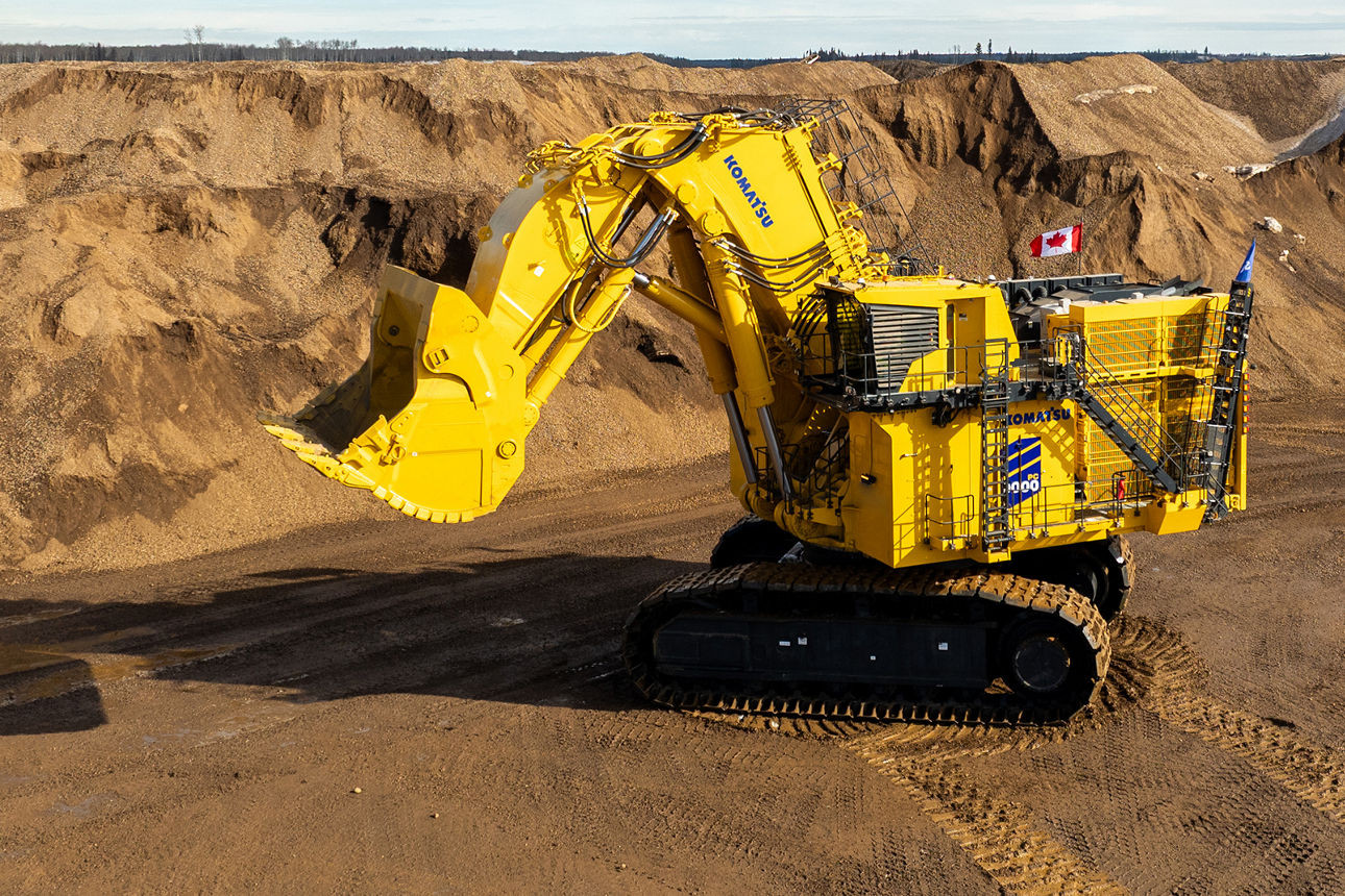 Komatsu PC9000-12 hydraulic mining excavator operating at a mine with large bucket and tracked undercarriage.