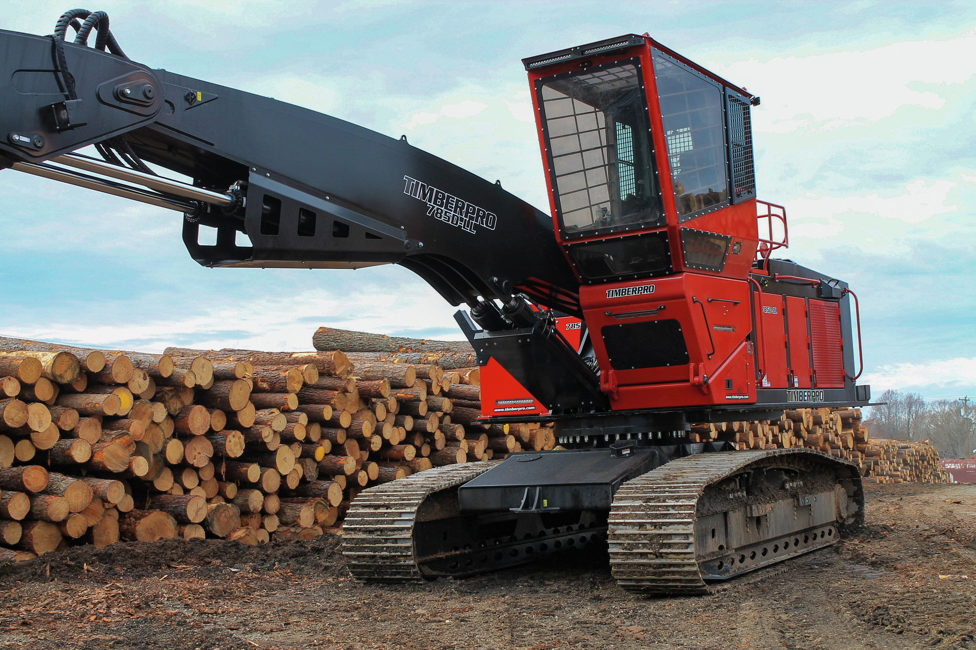 Left side view of a red and black Komatsu TN785D timberpro parked next to a long stack of wooden logs.