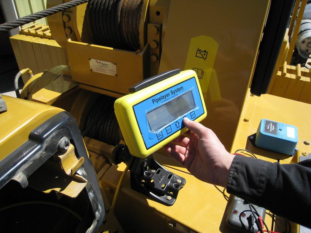 A button on a load monitor indicator panel is being pressed, panel features the text "Pipelayer System."