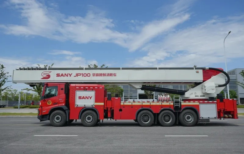 Red and White SANY JP100 Firefighting Water Jet Truck traveling on a road with a building behind it.