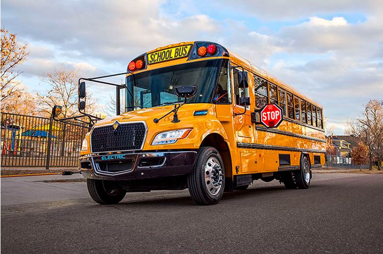 Left and front view of a yellow school bus with a stop sign extended out while parked on the pavement.