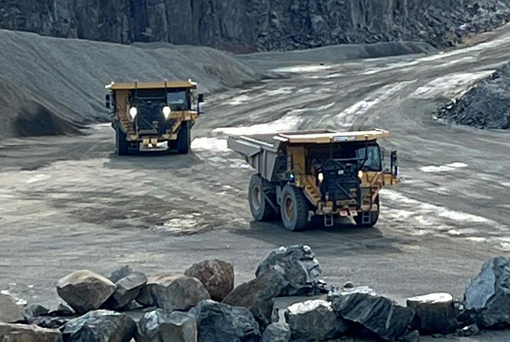 Two Cat 777 off-highway trucks operating on site with large rocks off to the side.