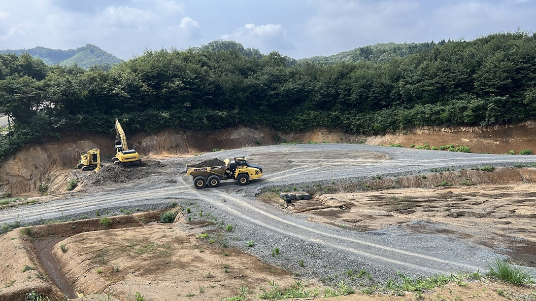 Komatsu HM400 articulated dump truck hauling dirt on a construction site while excavators work behind it.