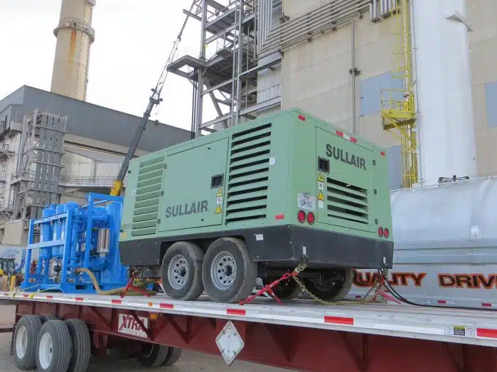 Green Sullair Air Compressor on a truck flatbed with buildings next to it.