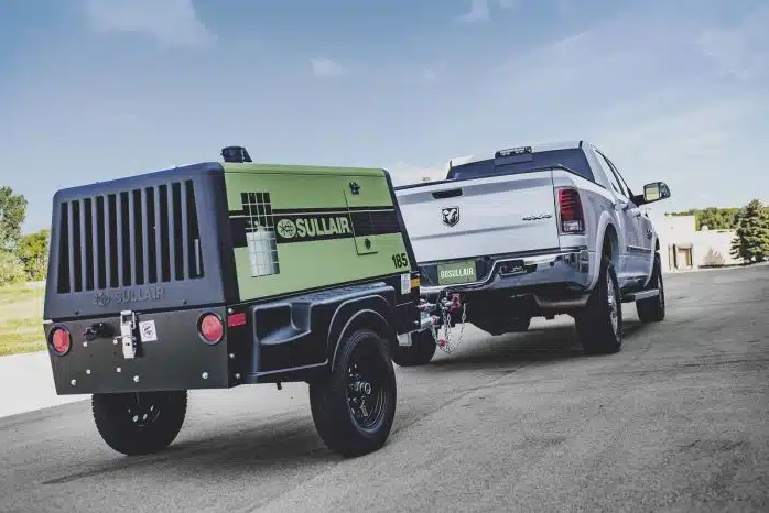 White Dodge pick up truck towing a green and black Sullair air compressor on a road.